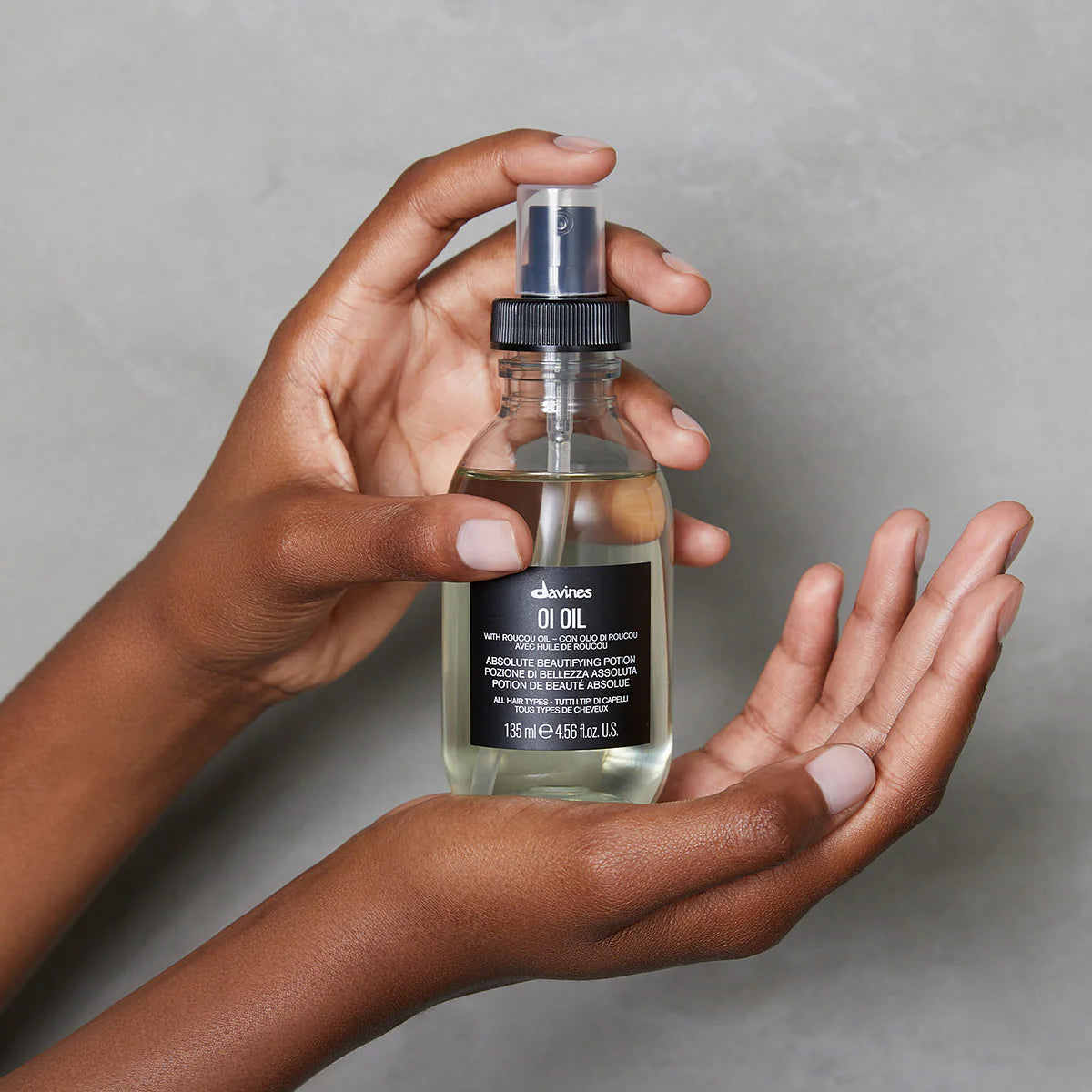 Hand holding a bottle of Davines OI Oil 135 ml with roucou oil for all hair types against a neutral background